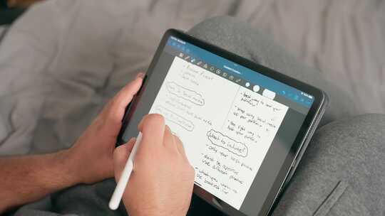 内容创作者、学生或自由职业者在iPad桌子上做笔记和数字规划的特写镜头