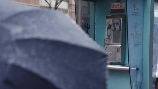 下雨天上海南京路电话亭旁行人撑伞走过