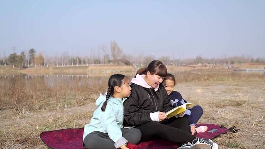 冬季在公园草坪上看书的母亲和两个女儿