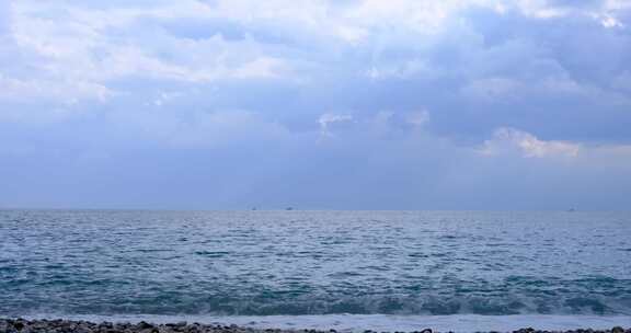 多云天空下到达海岸的海浪