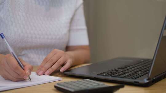 妇女使用计算器管理家庭支出在笔记本电脑上付款