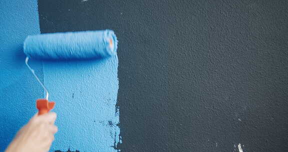 特写女人手持油漆滚筒，进行家庭修复墙壁重新粉刷