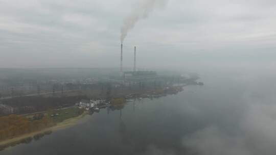 雾天空中，水边的发电厂工厂冒出浓烟