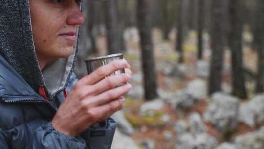 森林中年轻女子徒步旅行者用金属杯喝茶的特写肖像