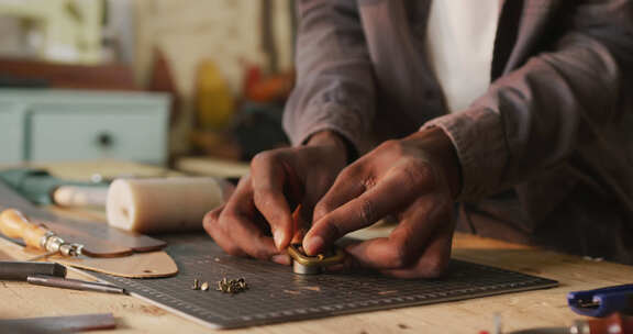 非裔美国工匠的手在皮革车间使用工具制作腰带