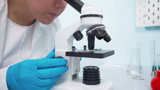 女医学研究科学家通过显微镜观察。