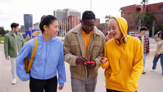 三个学生在高中外滑稽地散步使用手机城市快