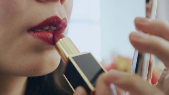女人拿着化妆镜描口红的特写