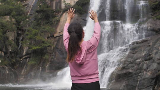 亚洲中国人女性在瀑布下张开双臂拥抱自然