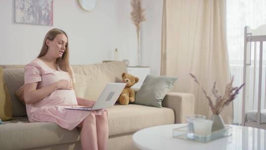 孕妇坐在沙发上抚摸着肚子看笔记本电脑视频素材模板下载