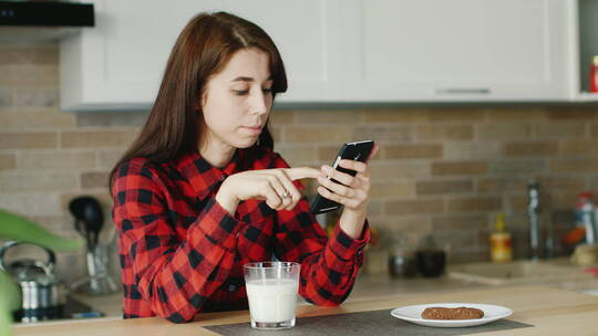 餐桌前喝牛奶和玩手机的女孩