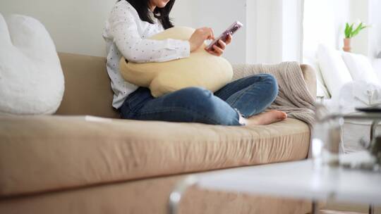 周末早晨年轻女孩坐在客厅沙发上玩智能手机视频素材模板下载