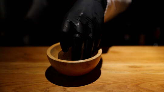 酒保把一个冰块放在一个木碗里，从摇壶里倒一杯饮料到一个精心准备的酒里
