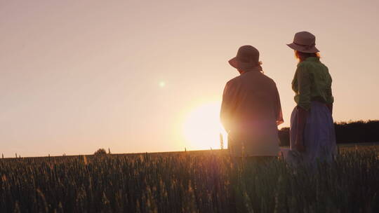 母亲和女儿看着麦田上美丽的日落