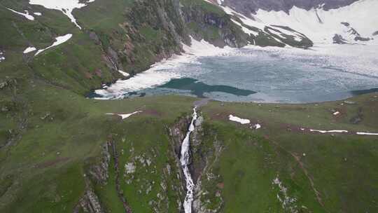 高山冰川湖，周围有绿色山丘和从湖中流出的