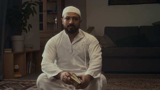 大胡子穆斯林男子在家拿着古兰经摆姿势的肖