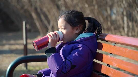 坐在公园长椅上休息喝水的女孩