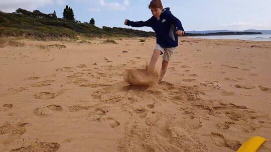 赤脚男孩踢海滩上的沙子