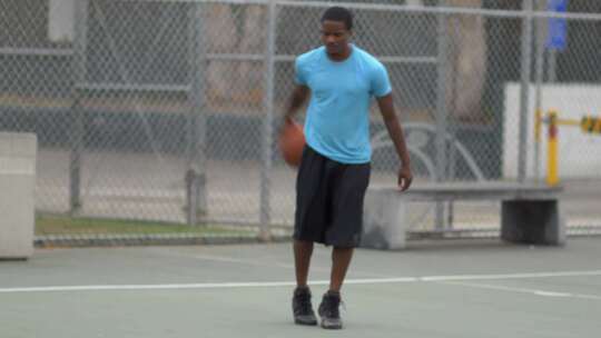 在室外球场上运球的年轻男子篮球运动员。