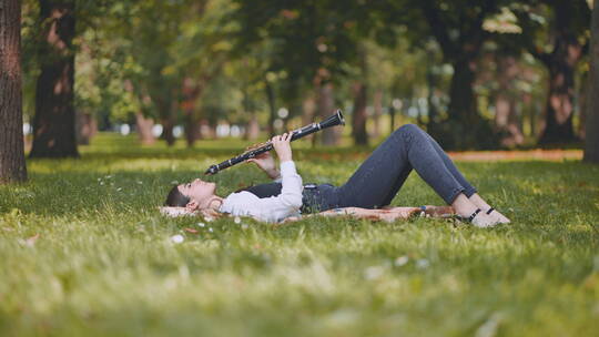 女孩躺在公园的草地上吹单簧管