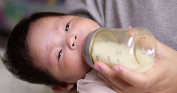 母亲用她妈妈拿着的奶瓶喂她的新生儿一些婴