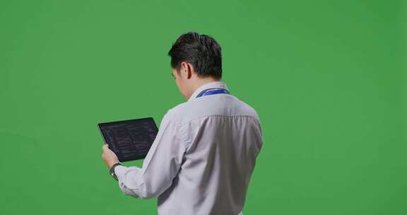 亚洲商人在绿屏背景前使用平板电脑