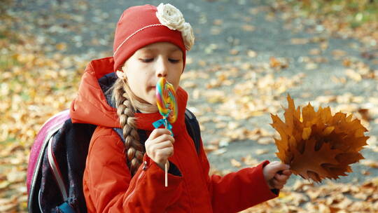女孩拿着秋天的树叶吃着棒棒糖