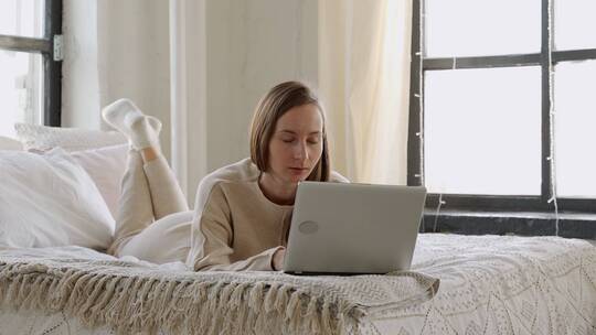 女人趴在床上看着笔记本电脑做出惊讶动作视频素材模板下载