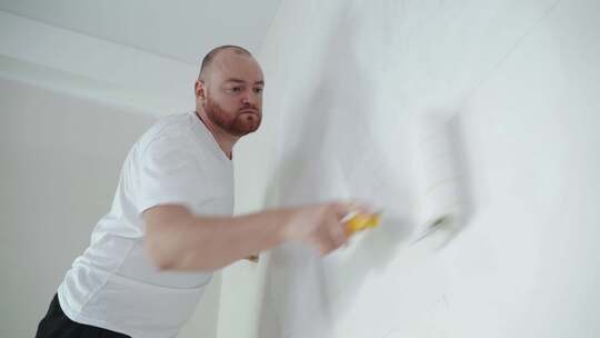 男人用滚筒粉刷白墙。内部维修。年轻的男性装饰师粉刷墙壁