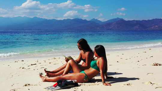 两个女孩坐在异国情调海滩的白沙上计划她们的旅行，阅读信息传单