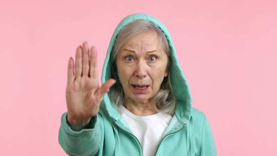 谨慎的老年妇女举着停止手掌标志绿色连帽衫