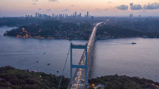 日落时的伊斯坦布尔博斯普鲁斯海峡大桥，配有汽车交通灯和城市天际线，空中超高速摄影视频素材模板下载
