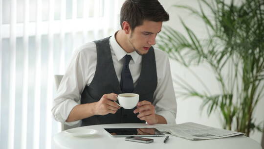 男人坐在桌旁看报纸喝咖啡