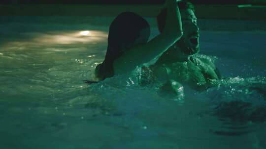 女人在绿色灯光的游泳池里把男人浸泡在水下
