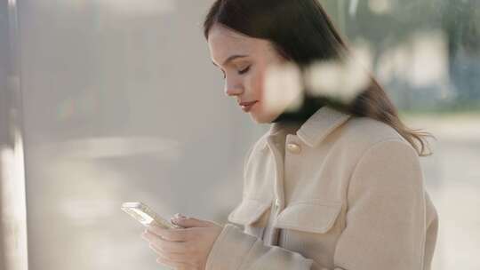 年轻女子在公共汽车站等候时使用智能手机