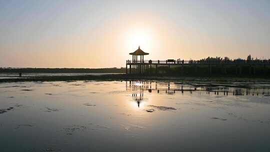 夕阳下海边退潮后滩涂与亭子剪影