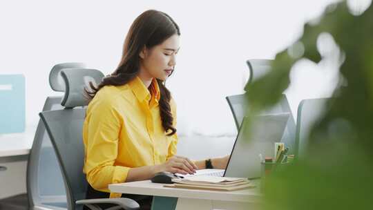 穿着黄色衬衫喝咖啡的亚洲女人用电脑笔记本电脑思考得到想法