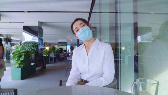青年女人戴着口罩坐在咖啡馆里视频素材模板下载