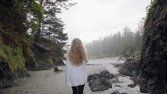 阴天，女人走在森林边的沙质河岸上