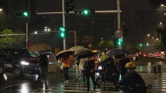 夜晚下雨天的行人及马路交通和街边暴雨场景
