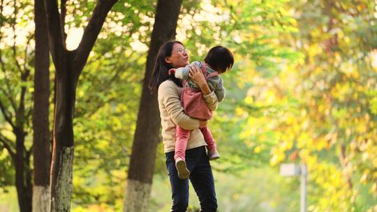 妈妈抱着女儿在秋天阳光灿烂的公园里玩耍