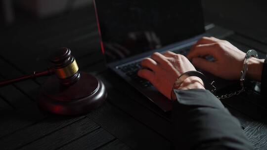 审讯室嫌疑犯双手戴着手铐操作电脑和法槌视频素材模板下载