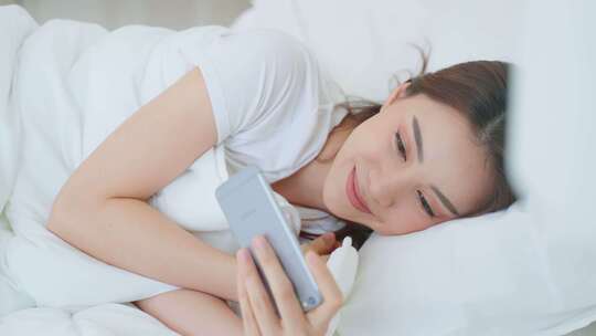 女人躺在床上微笑的看着手机