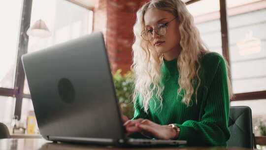 金发女子使用笔记本电脑工作坐在咖啡馆的桌子上自由职业者使用免费Wifi肖像拍摄