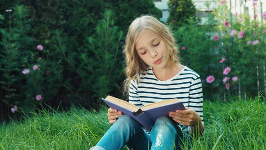 漂亮的女孩坐在草地上看书