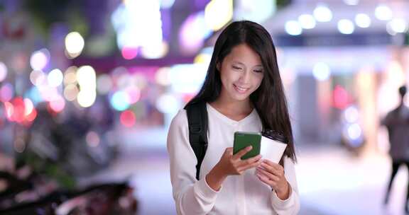 亚洲妇女在台北晚上拿着咖啡纸杯使用手机