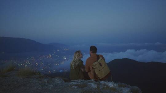 情侣坐在山坡看晚上城市