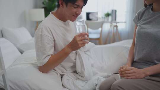 亚洲妻子躺在床上给丈夫喂药和水。