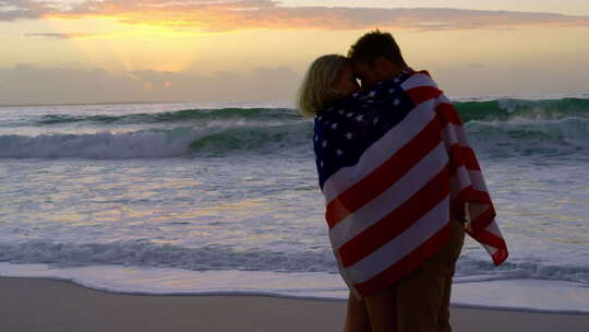 日落时，海滩上裹着美国国旗的夫妇4k
