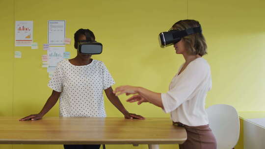 两个不同的女同事站在办公桌前，测试虚拟现实谷歌